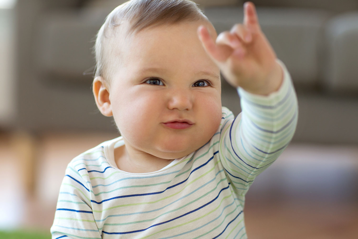 baby is striped shirt with their left hand up to make a sign
