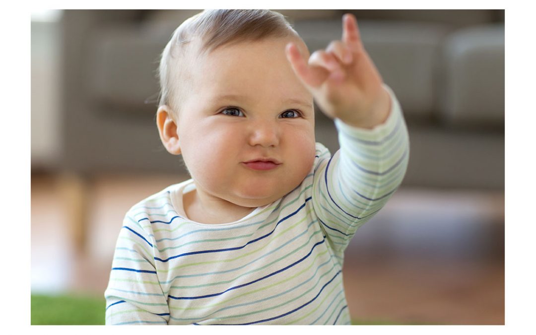 baby in striped shirt is holding hand up to use sign language