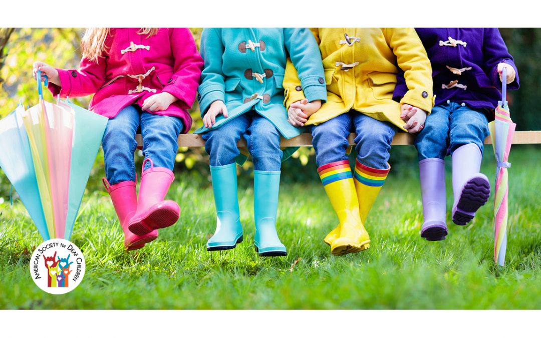 children in colorful raincoats and rain boots sitting on a bench holding hands